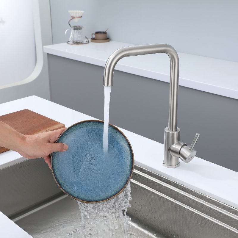 Robinet de cuisine en nickel brossé, bec à grand arc, design moderne. L'eau coule dans une plaque bleue dans un évier en acier inoxydable.