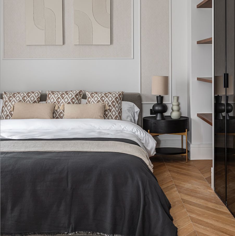 Chambre avec parquet massif chêne français – Point de Hongrie, lit avec couverture noire et table de chevet avec lampe.