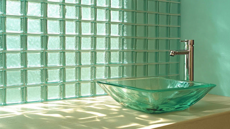 Les briques de verre dans une salle de bain avec vasque en verre et robinet chromé.