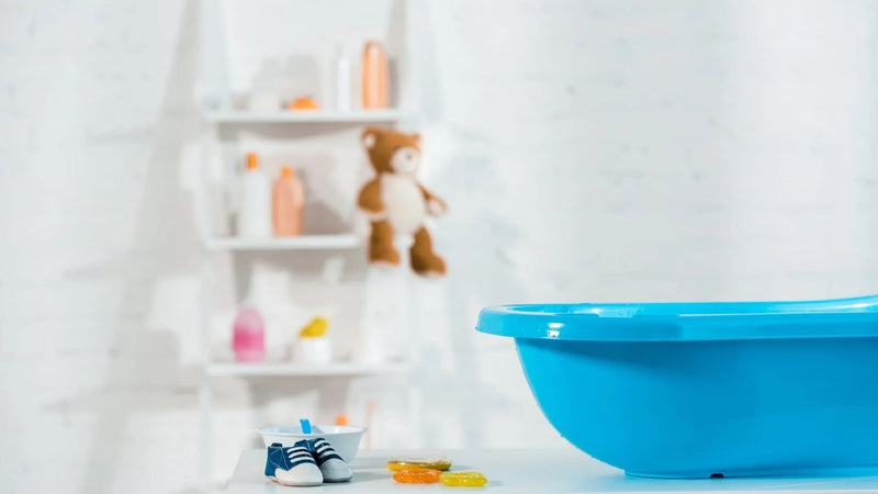 Baignoire bébé bleue sur table, avec étagère, chaussures et produits de bain en arrière-plan. Préparation de la salle de bain pour bébé.