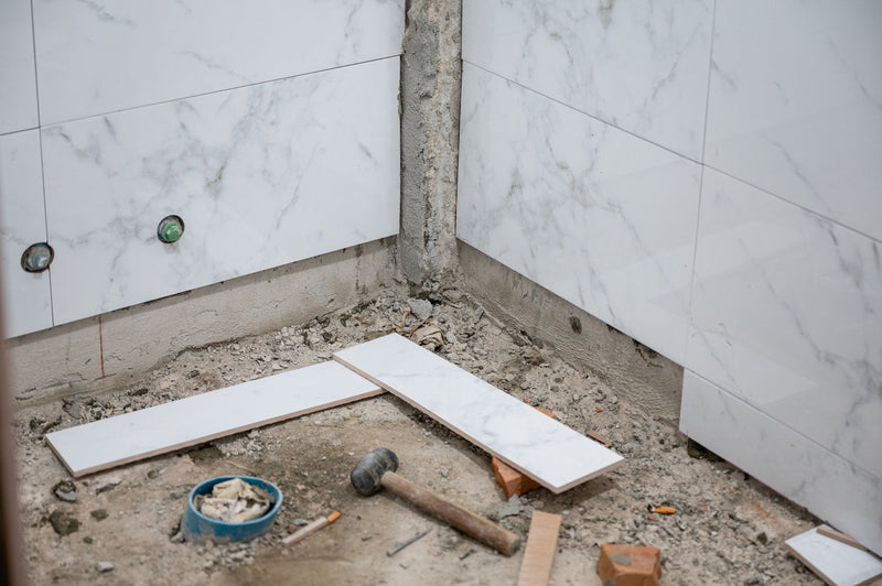 Pose de carrelage marbre dans une salle de bain en cours : outils et matériaux sur le sol.