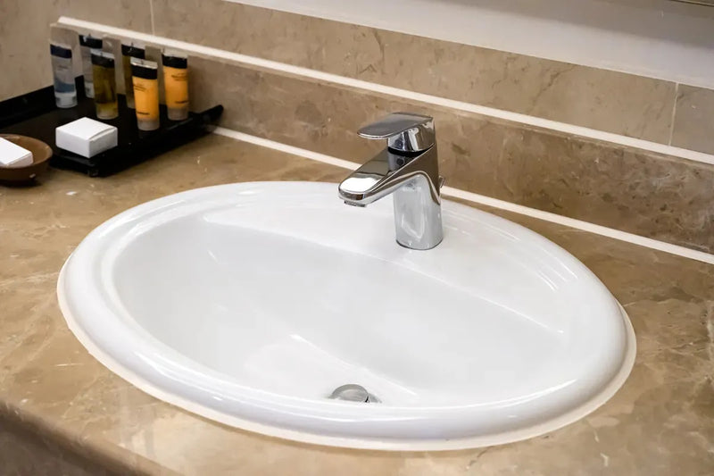 Vasque blanche ovale encastrée sur un plan de travail en marbre. Design moderne et élégant.