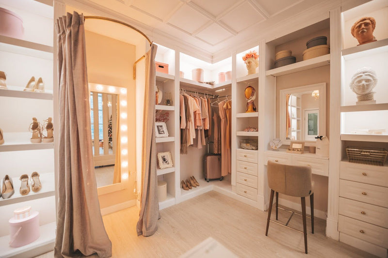 Dressing luxueux avec éclairage, miroirs, et vêtements roses suspendus. Aménagement intérieur élégant.
