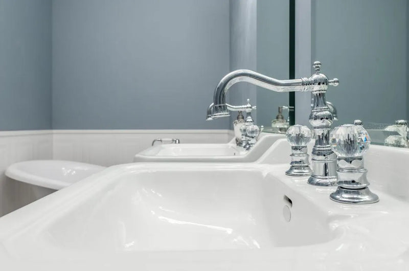 Robinet de lavabo chromé avec poignées en cristal, sur un lavabo blanc.