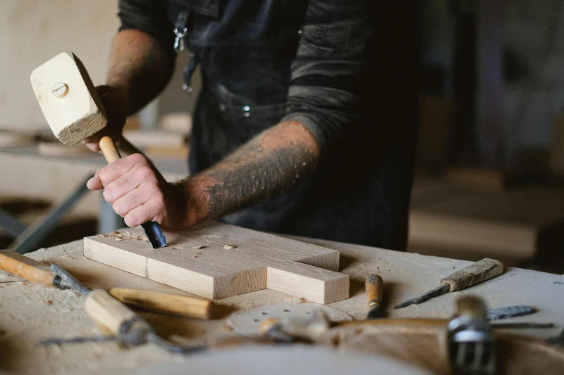 Artisan menuisier travaillant le bois avec ciseau et maillet, préparation pour travaux de menuiserie.