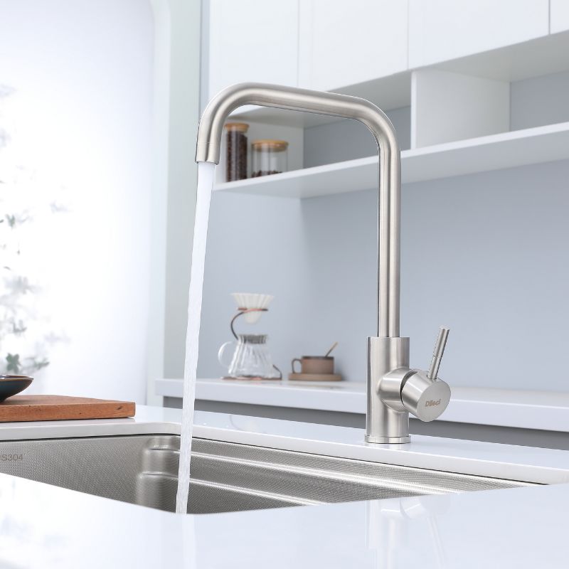 Robinet de cuisine en nickel brossé, design à grand arc, style moderne et intemporel. L'eau coule dans un évier en acier inoxydable.