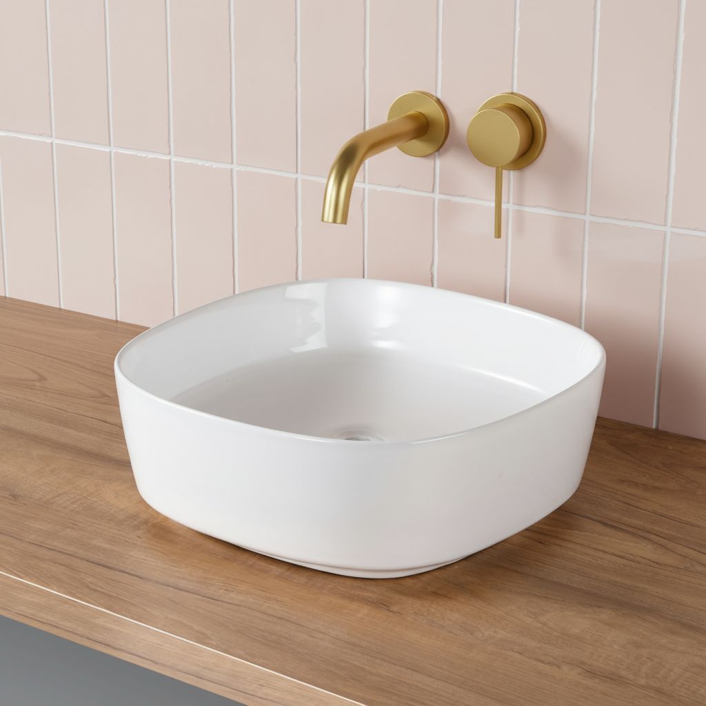 Vasque carrée arrondie blanche sur comptoir en bois avec robinet doré.